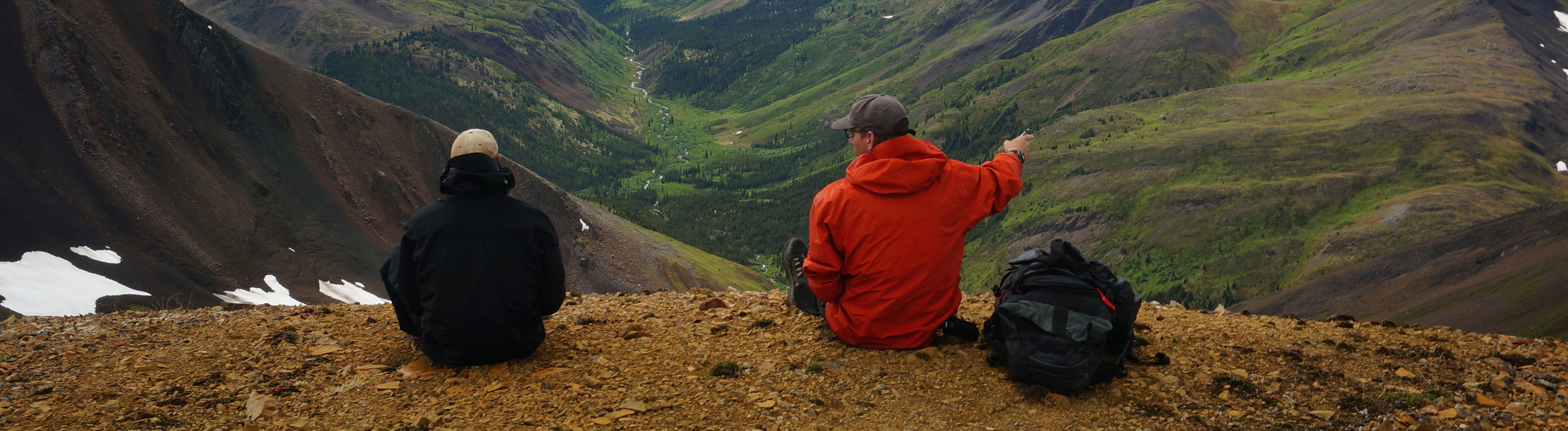 Professor Eric Sperling sits with a student overlooking a valley and gestures to his right