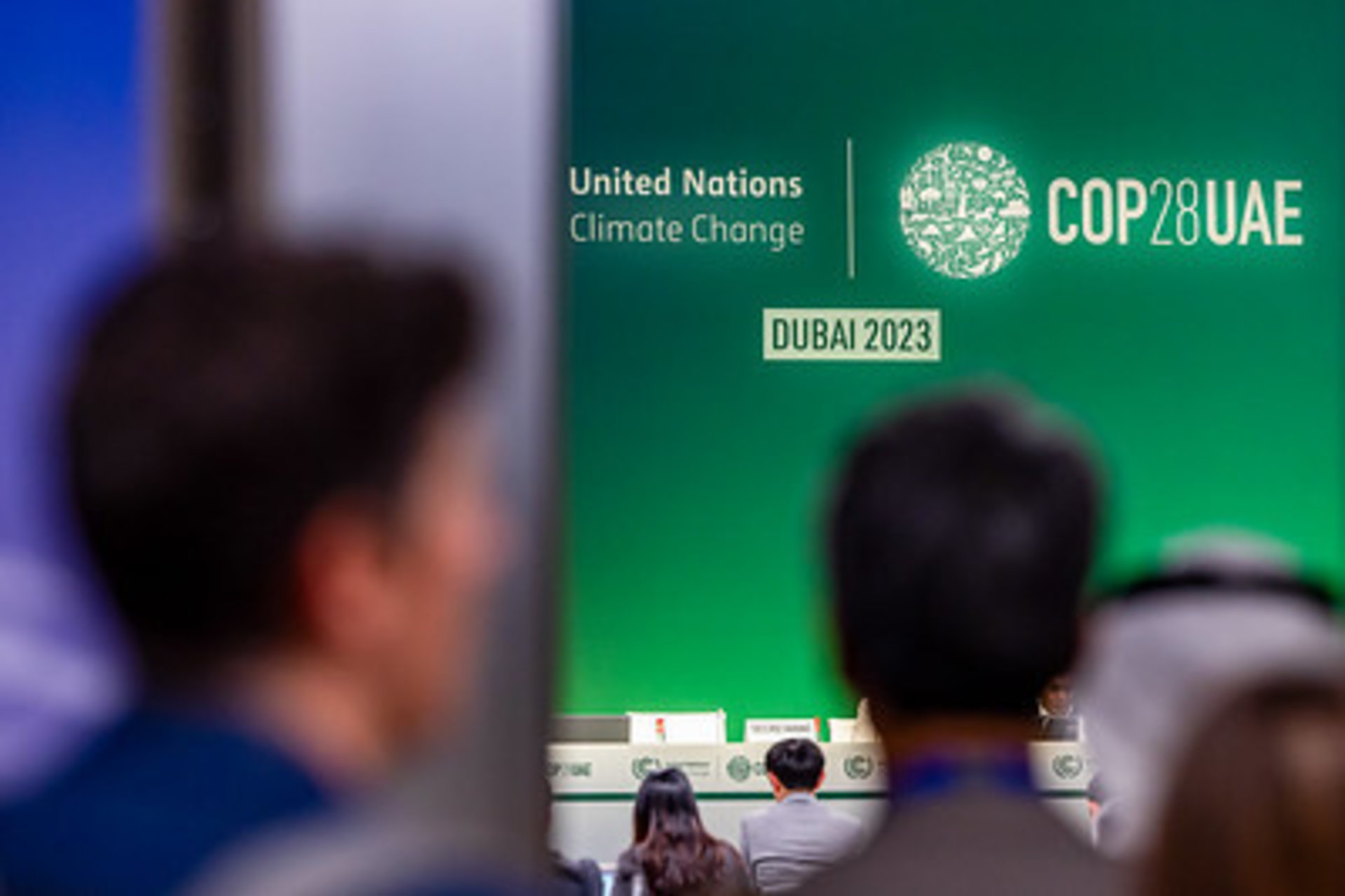Two people look toward a stage with COP28 Dubai signage