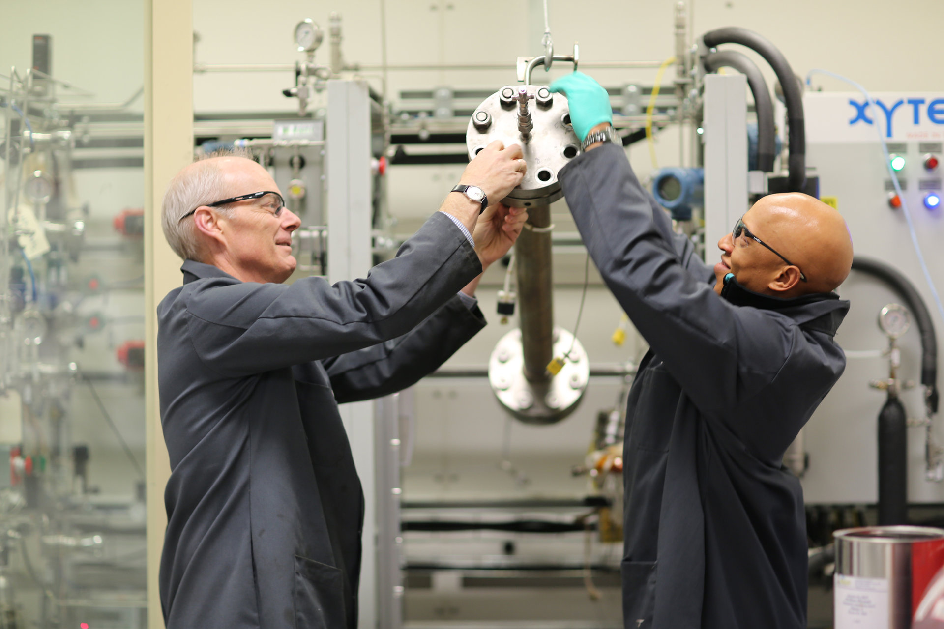 Two researchers assist each other as they lift a piece of complex machinery in a lab