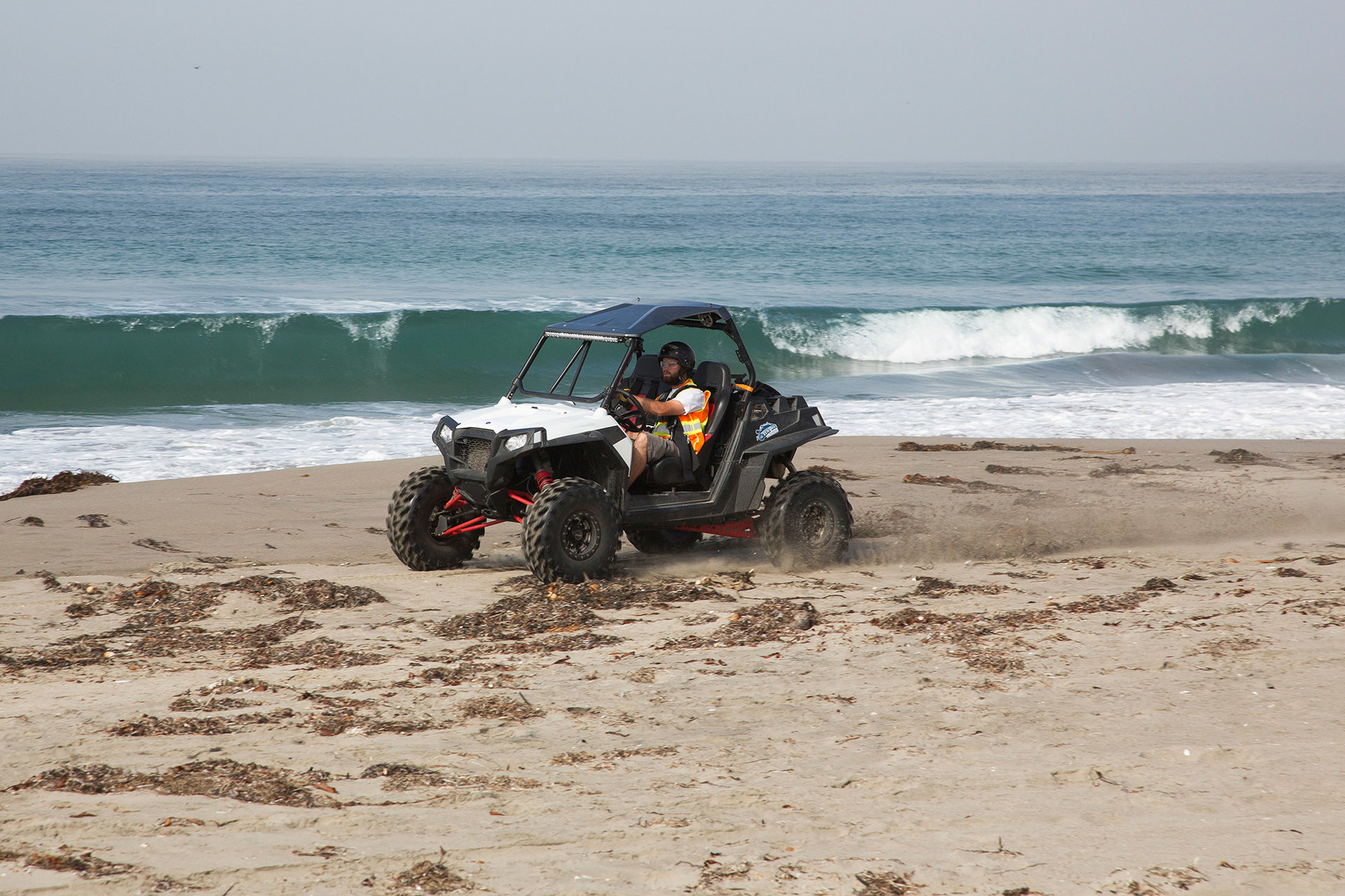 A student drives a four wheeler along a beach wearing proper safety equipment