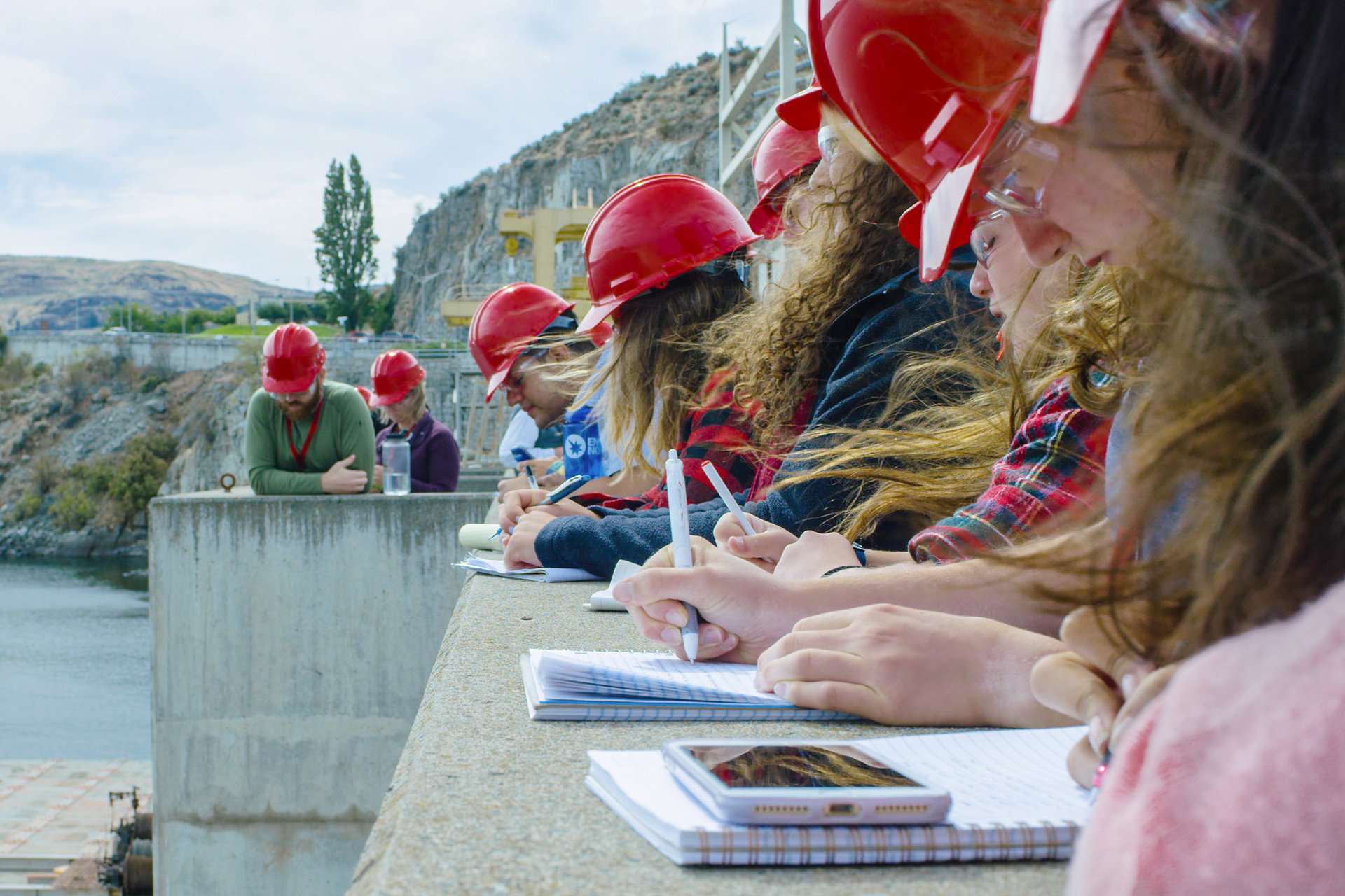 Students wearing hardhats and taking notes at a dam