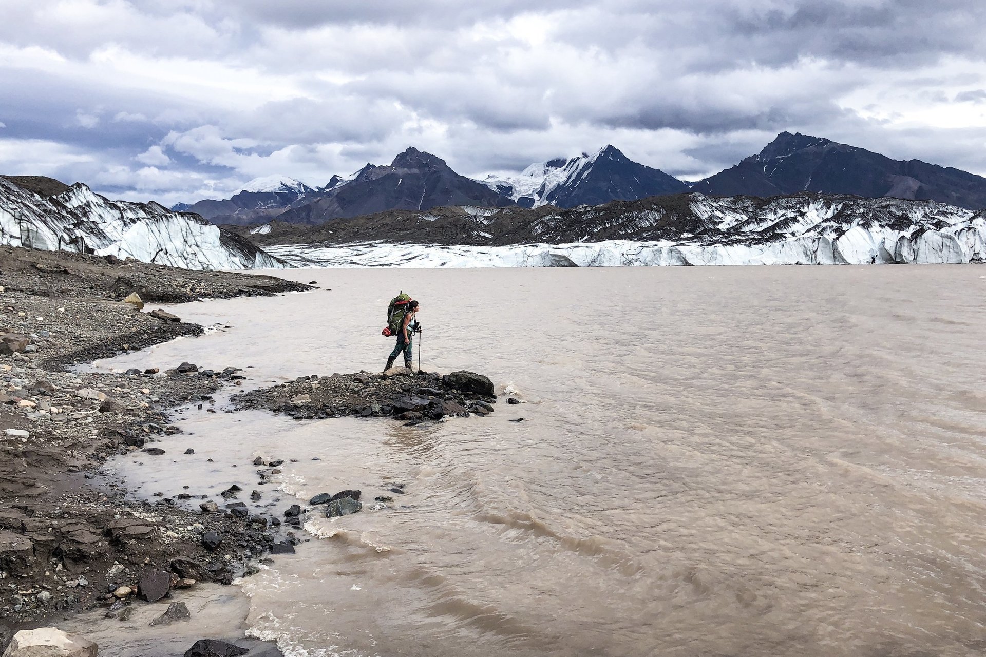 woman hiking by glacier with mountains in background