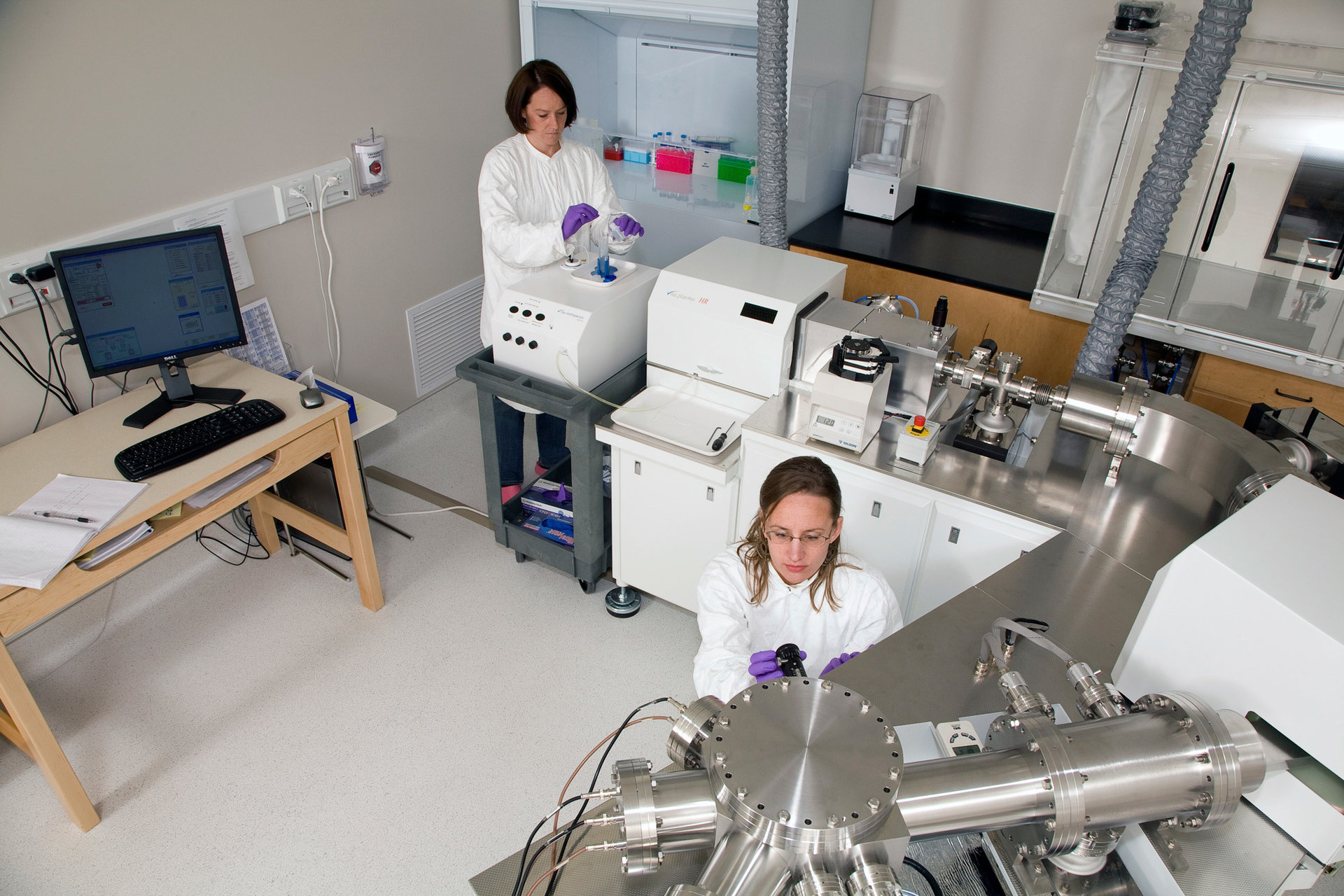 Two researchers in the Maher lab wearing lab coats and gloves as they perform their work
