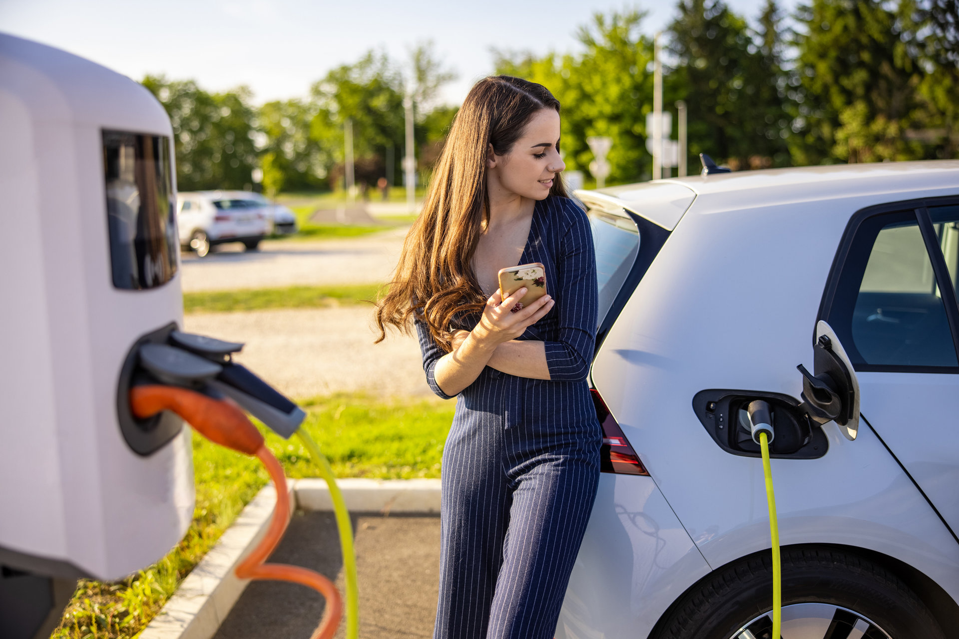 A woman holding a cell phone waits for an electric car to charge