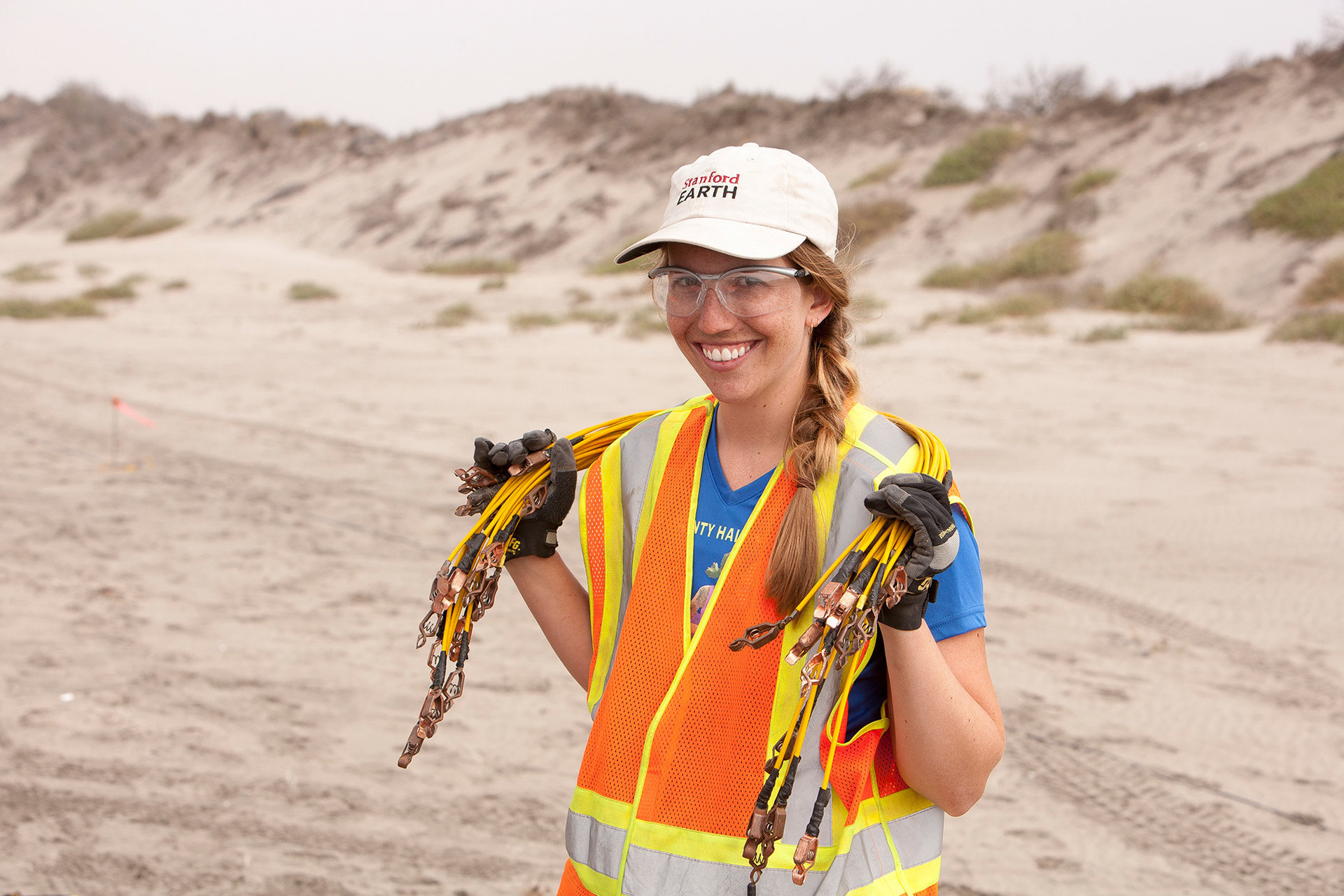 A female student wearing a safety vest and hat as she holds a bundle of cables around her shoulders