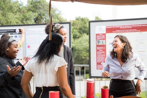 Four female students laugh with each other at a poster session