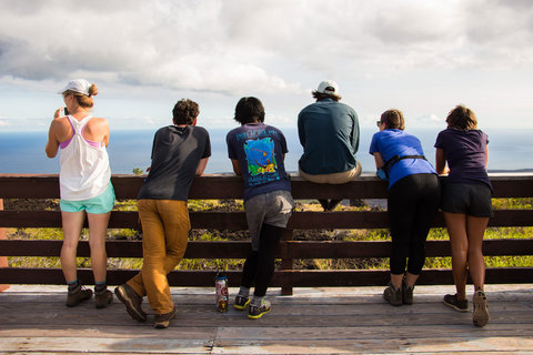 Six different students lean across a railing overlooking the ocean on a trip in Hawaii